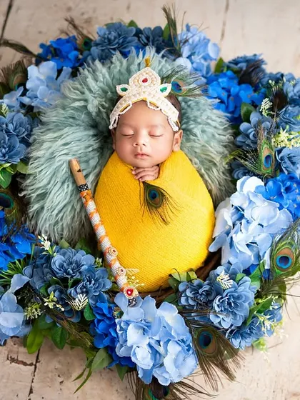 Even the tiniest newborns can join the celebration. This sleeping baby is swaddled in yellow and posed as little Krishna with a flute and peacock feathers in a floral nest.