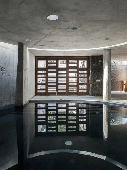 The subterranean pool at K-Lagoon is a serene, contemplative space. Circular skylights in the concrete ceiling cast soft light onto the dark water, creating a tranquil atmosphere.