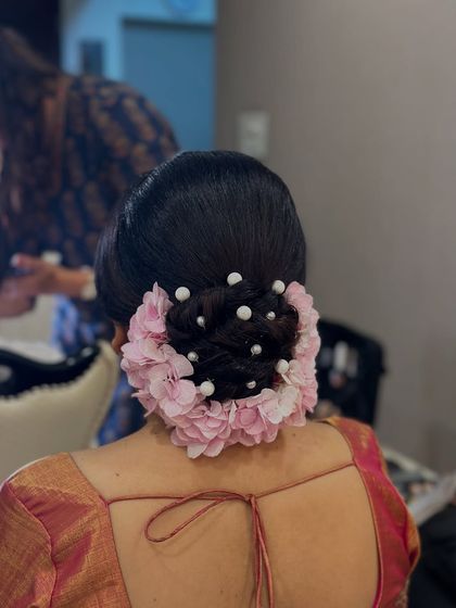 A beautiful bridal bun adorned with a halo of pink flowers and scattered pearl pins. This is a popular choice for brides who want a romantic and feminine look.