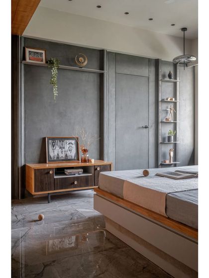 This bedroom features a minimalist design with a focus on clean lines and functional furniture. The wall is treated with a cool grey texture, providing a calm backdrop for the simple wood furniture and open shelving.