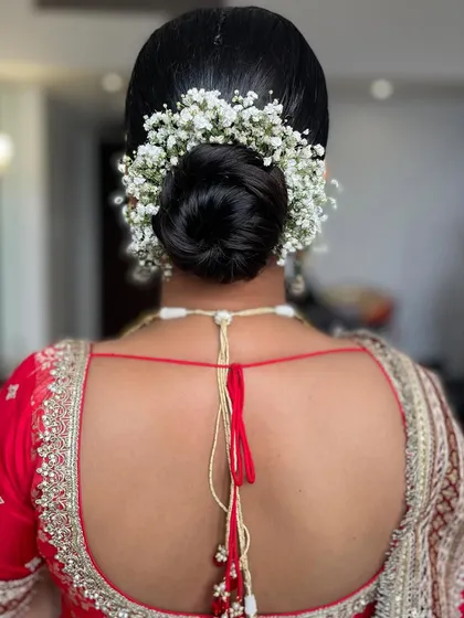 A soft, twisted low bun adorned with a halo of delicate baby's breath. This style is perfect for a romantic, traditional look for a wedding or engagement ceremony.