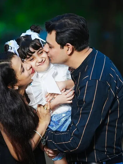 A heartwarming moment of family affection, with both parents kissing their daughter's cheeks during a sunny outdoor session.