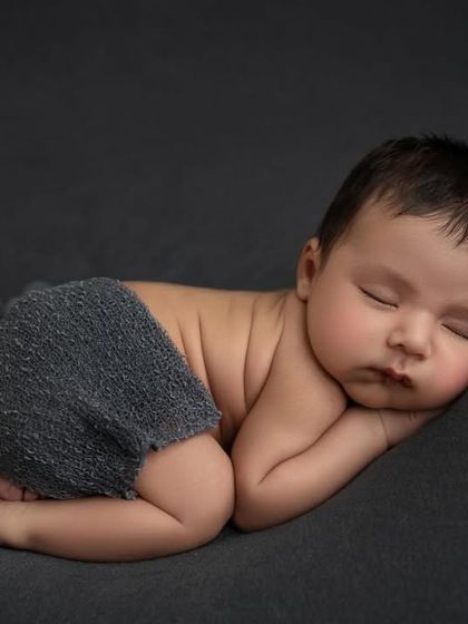 The 'taco' pose on a dark grey background, with the baby's back and tiny feet visible. This pose mimics how they were curled up in the womb.