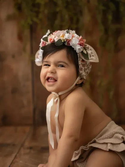 A happy baby girl wearing a beautiful floral bonnet. These sweet accessories can add so much charm to a baby photoshoot.
