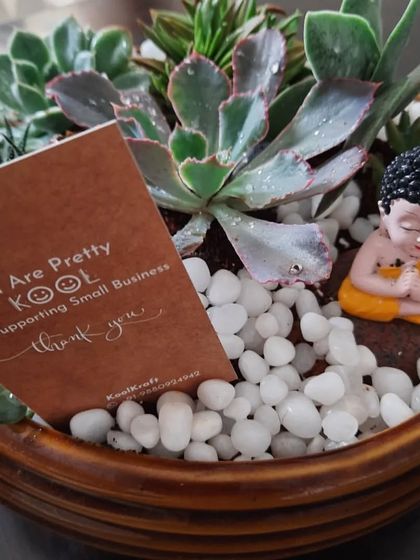 A close-up of a succulent Zen garden I made as a thank you gift for a client. It includes a variety of succulents, white pebbles, and a small meditating monk, along with a personal note.