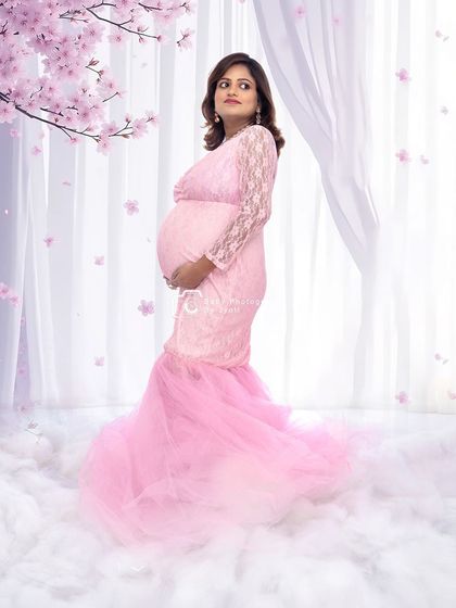 A dreamy portrait in a pink mermaid gown, standing on a bed of clouds with cherry blossoms in the background.
