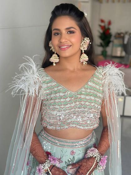 Mehendi, but make it glam! This look features a fresh, dewy base with peachy tones and soft smokey eyes to complement a modern pastel lehenga with feather details.