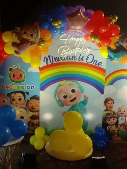 A Cocomelon first birthday party with a rainbow backdrop. This setup includes a colorful balloon arch and a marquee number '1'.