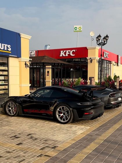 A sleek black Porsche and Toyota Supra parked outside our KFC. We offer endless flavors for every kind of driver.