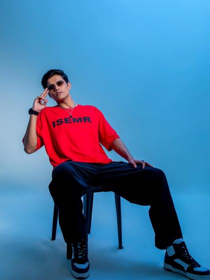 A relaxed yet confident pose in a studio setting with a cool blue background. The styling of this red graphic tee with black pants and high-top sneakers is simple, effective, and commercially appealing.