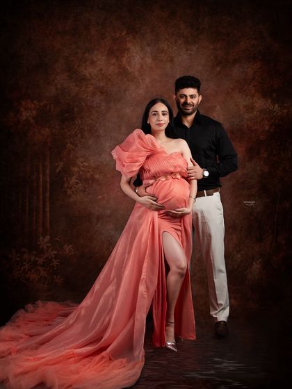 A classic couple portrait against a rich, brown backdrop. The client's peach gown and her partner's dark shirt create a warm and elegant composition.
