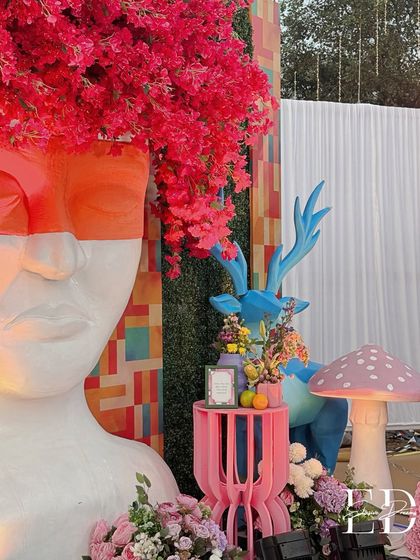 A wider composition showing how the large head sculpture, blue deer, and mushroom props create a layered and immersive scene.