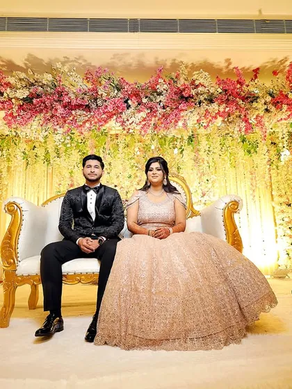 The couple seated on a grand stage, surrounded by a stunning floral arrangement. This captures the scale and beauty of their engagement celebration.