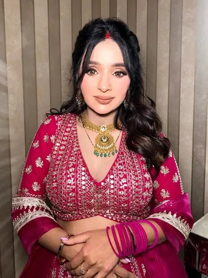 A close-up of the client in the magenta lehenga, her gold and emerald necklace adding a touch of color.