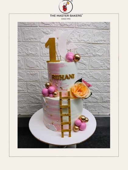 Celebrating a first birthday is a huge milestone. This beautiful two-tiered cake for Ruhani features soft pink and white tones, a golden ladder, and balloon accents, symbolizing the climb into a new year.
