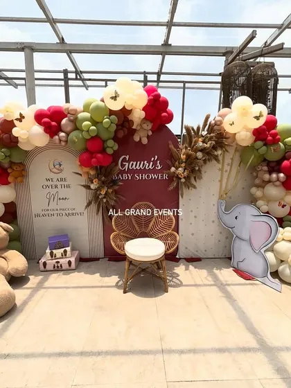 I create beautiful and memorable setups for milestones like baby showers. This 'Over the Moon' theme includes a custom backdrop, an elegant balloon arch in earthy tones, and adorable props like teddy bears and a wicker peacock chair for the mom-to-be.
