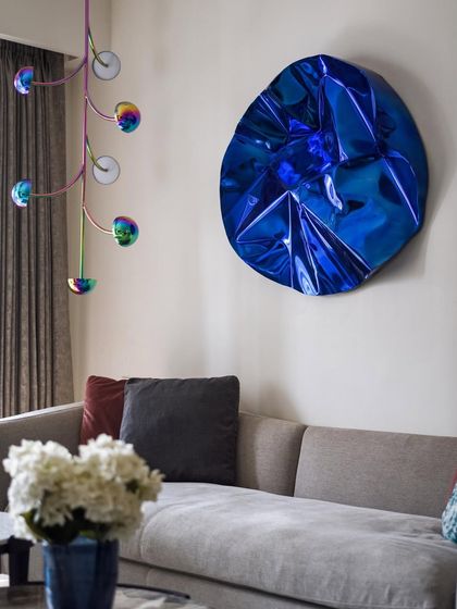 A stunning blue metallic art piece by Hitesh Gilder and a quirky, iridescent pendant light by Hatsu are the highlights of this living room. They add a playful yet sophisticated pop of color and form to the neutral space.