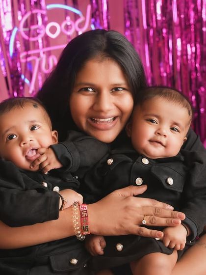 Double the love, double the joy. A proud mother holds her twin babies, their coordinated outfits and happy faces making for an absolutely adorable family portrait.