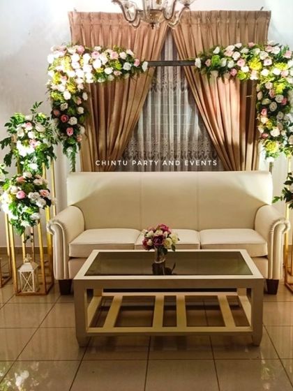 An elegant Catholic wedding stage decoration for a home ceremony. The setup uses a floral arch over the main sofa, with matching flower stands.