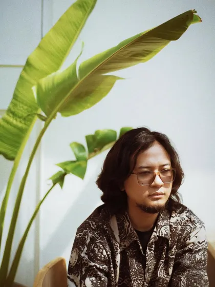 A portrait of Taba Chake in a cafe, surrounded by greenery. The natural elements add a sense of calm and tranquility to the shot.
