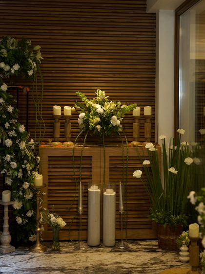 A beautifully styled console table combining modern and rustic elements. The setup features white and green floral arrangements, candles, and a wooden cabinet, creating a sophisticated welcome area.