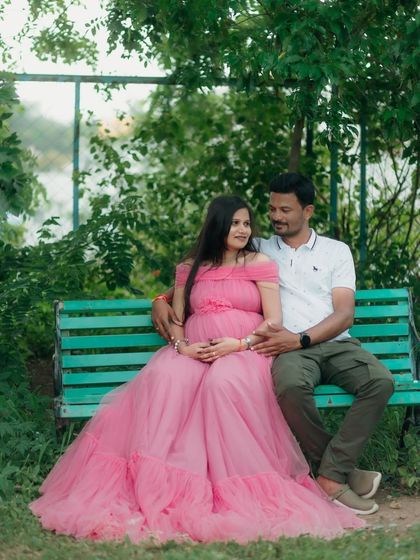 A sweet and relaxed couple's maternity photo. The soft pink tulle gown spreads out beautifully, adding a touch of elegance even in a casual park bench setting.