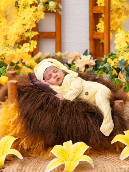 A newborn in a yellow sleeper and cap rests on a bed of fur, surrounded by bright yellow flowers. This cheerful and sunny setup is perfect for creating warm and joyful newborn portraits.