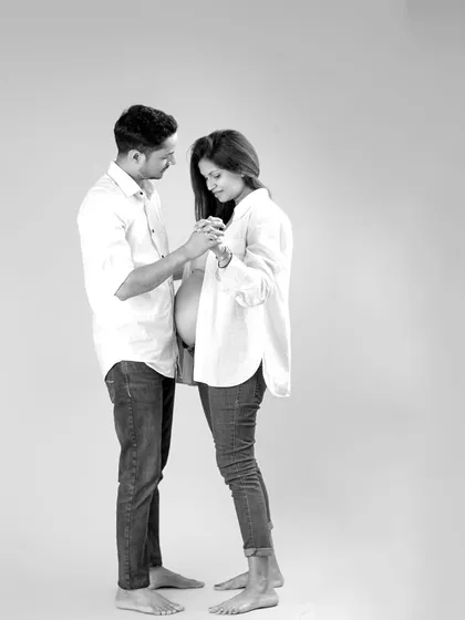 This black and white portrait captures a candid, gentle interaction between the expecting parents. Dressed in simple, coordinating outfits, their connection and the beautiful silhouette of the baby bump are the focus.