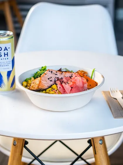 A point-of-view shot of a salmon bowl on a clean white table. This makes the viewer feel like they are about to enjoy the meal themselves.
