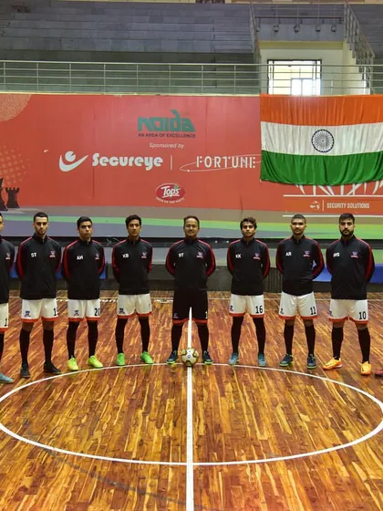 A futsal team lines up on the center circle in front of the Indian flag. We are a proud venue for national-level tournaments that celebrate sports and patriotism.