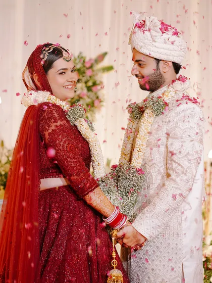 A beautiful candid moment from the wedding ceremony. The couple holds hands, surrounded by a shower of flower petals, their faces lit up with happiness.
