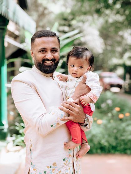 A father holds his son, both dressed in our custom designs. The father's embroidered jacket and the son's tiny kurta show how we scale our designs for the whole family.