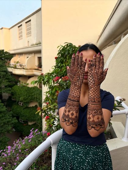 The classic "hiding face" pose, which beautifully showcases the full extent of the arm mehndi, featuring jaali work and traditional borders.