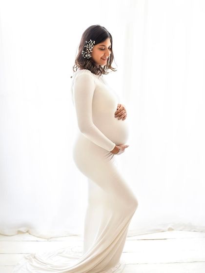 A classic and elegant silhouette. This mom-to-be is wearing a simple white gown with delicate hair accessories, creating a timeless and graceful maternity portrait.