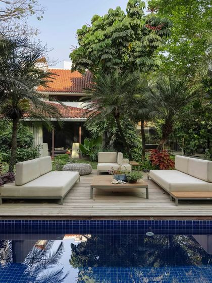 A poolside lounge area set on a timber deck, surrounded by mature palm trees. The symmetrical arrangement of the furniture creates a sense of order and calm, perfect for a resort-style backyard experience.