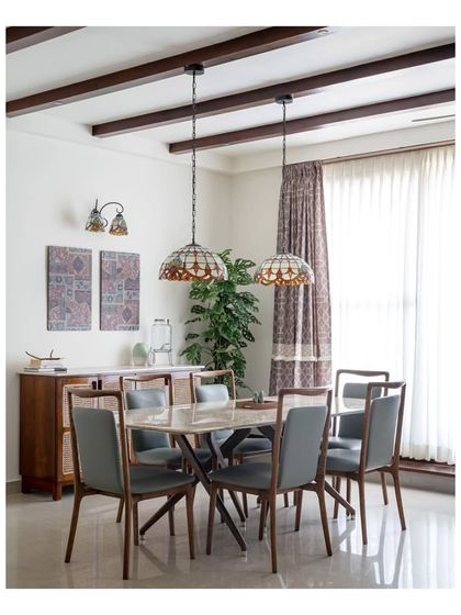 The dining area, featuring a stone-top table from Stanley and pleasant green leather chairs. The space is accented by a wooden console with rattan panels and beautiful stained-glass chandeliers.