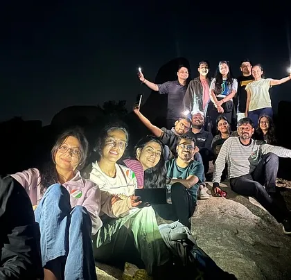 A group photo taken at night during the Anthargange trek, with headlamps and phone torches lighting up the scene.