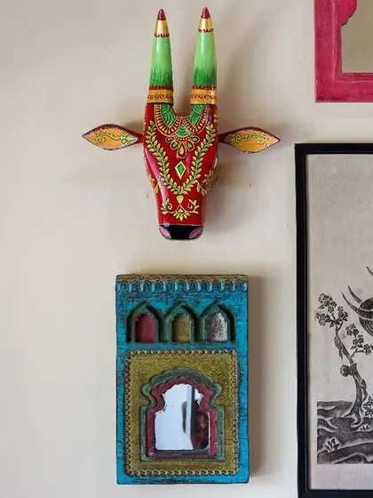 A close-up of a gallery wall featuring traditional Indian art and decorative mirrors, including a colorful, hand-painted cow head. This detail showcases the villa's eclectic and culturally rich decor.