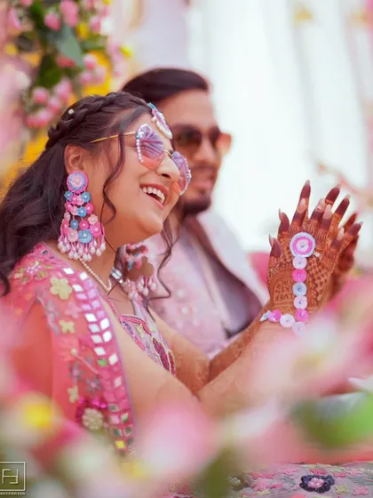 A candid moment of pure laughter. This shot, framed by flowers, captures the bride enjoying her Mehendi ceremony. It’s these unscripted, happy moments that make the best memories.