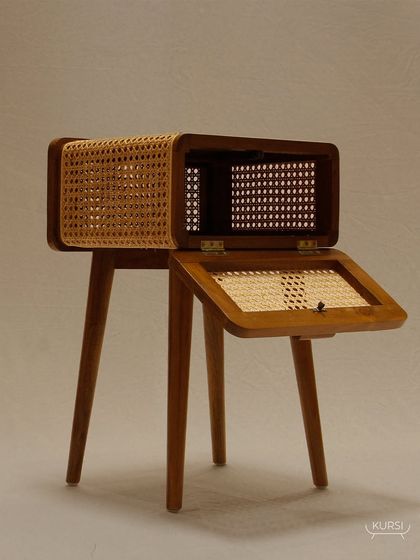 The 'Koshi' table with its top compartment open, revealing the thoughtful storage design and the beautiful contrast of teak and rattan.