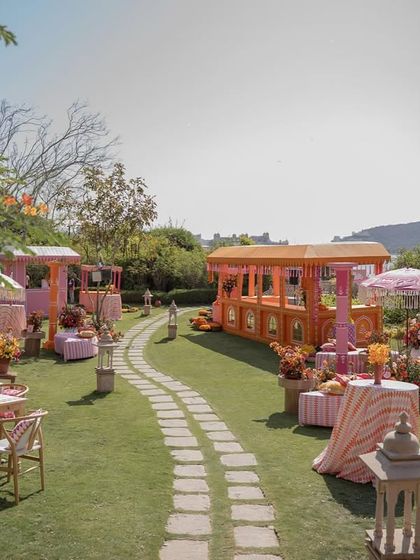 A winding stone path through the 'Pyaar ka Pind' setup, leading guests past colorful food stalls and seating areas, all with a view of the lake.