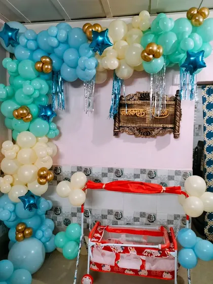 A home naming ceremony setup featuring a cradle decorated with a balloon arch in shades of blue, cream, and gold.