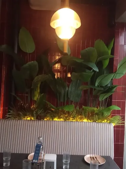 A cozy restaurant booth with a custom-lit planter box filled with artificial tropical plants. This creates an intimate and lush dining experience for patrons.