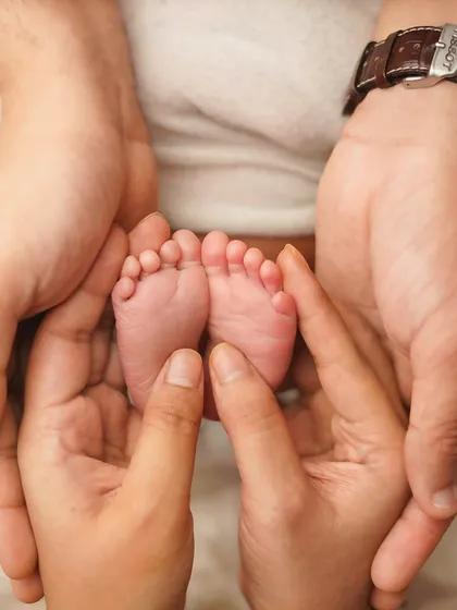Both parents' hands cradle their baby's feet, creating a frame of love and protection. This is a family portrait of a different, equally meaningful kind.