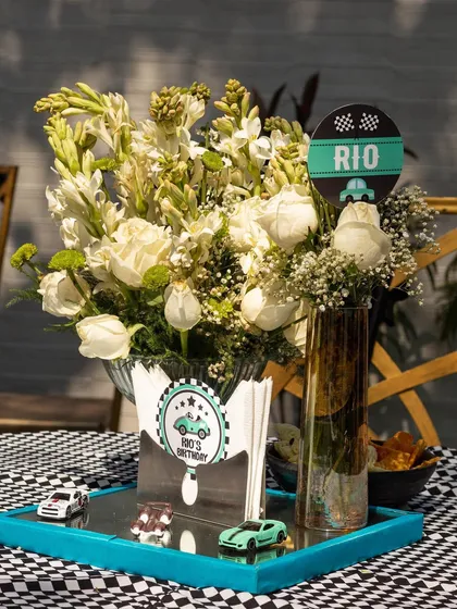 Themed table centerpieces for Rio's racing birthday. Every detail, from the checkered-flag napkins to the toy cars, is thoughtfully curated to match the theme.