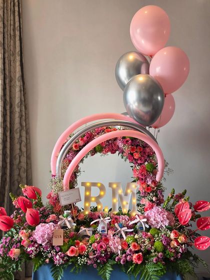 A breathtaking floral arrangement with personalized light-up initials 'RM', surrounded by pink and silver balloons, creating a truly grand gesture.