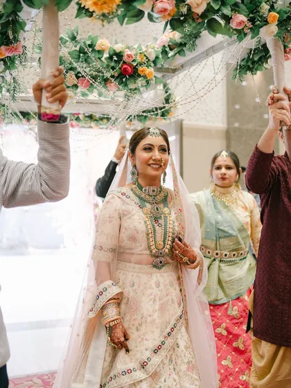 The bride's grand entrance under a floral 'phoolon ki chadar'. She looks like a princess, with her elegant pastel lehenga and glowing makeup.