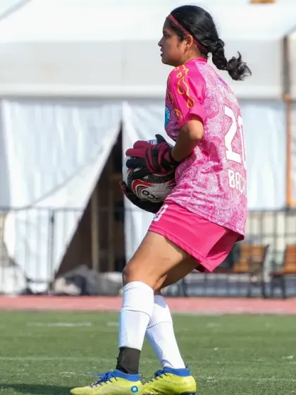 Our goalkeeper in her bright pink kit, ready and focused, holding the ball securely.
