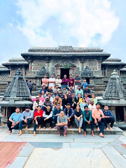 A large group seated on the steps of a beautifully carved Hoysala temple. These sites provide a stunning backdrop for group photos and a deep dive into Karnataka's history.
