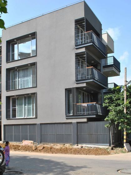 The full facade of the Gurgaon residence. The arrangement of windows and balconies creates a rhythmic pattern, while the dark steel elements provide a strong graphic contrast against the neutral grey mass of the building.